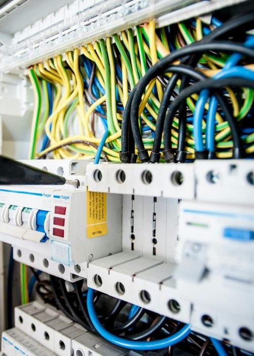 Hand of electrician working on a circuit breaker panel with colorful wires, ensuring safe electrical connections.